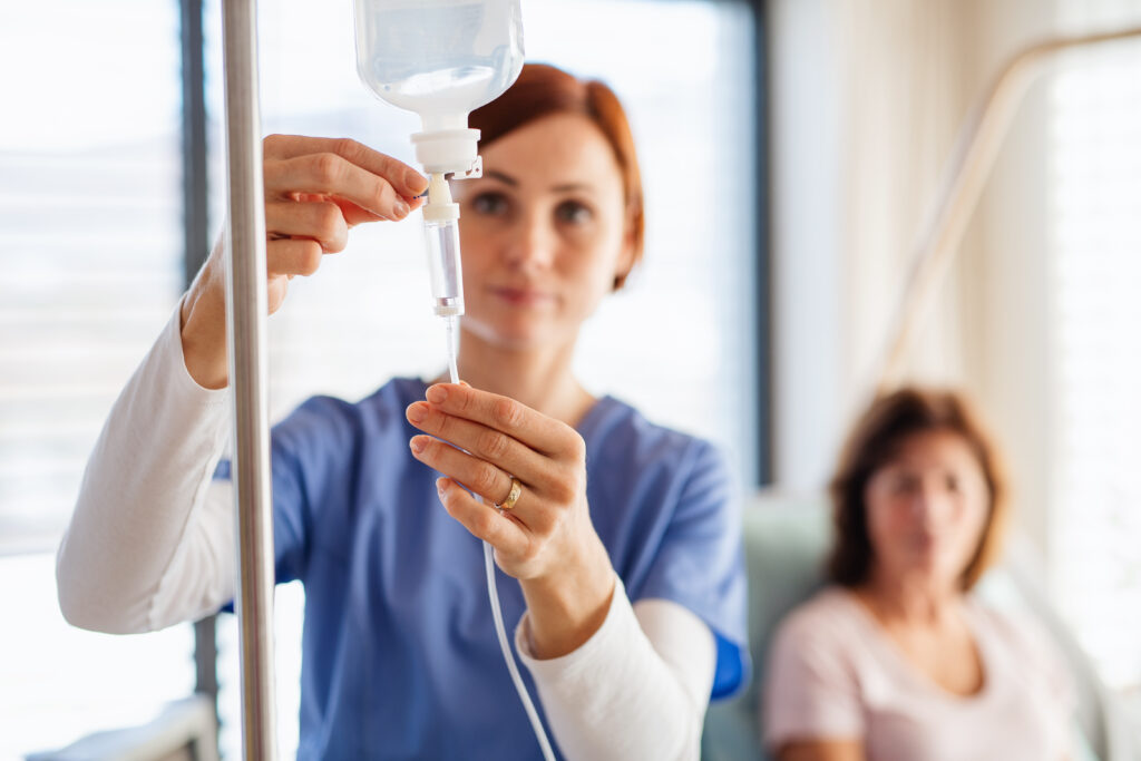 A nurse with IV drip and patient in bed in hospital room- Vitals Health Care