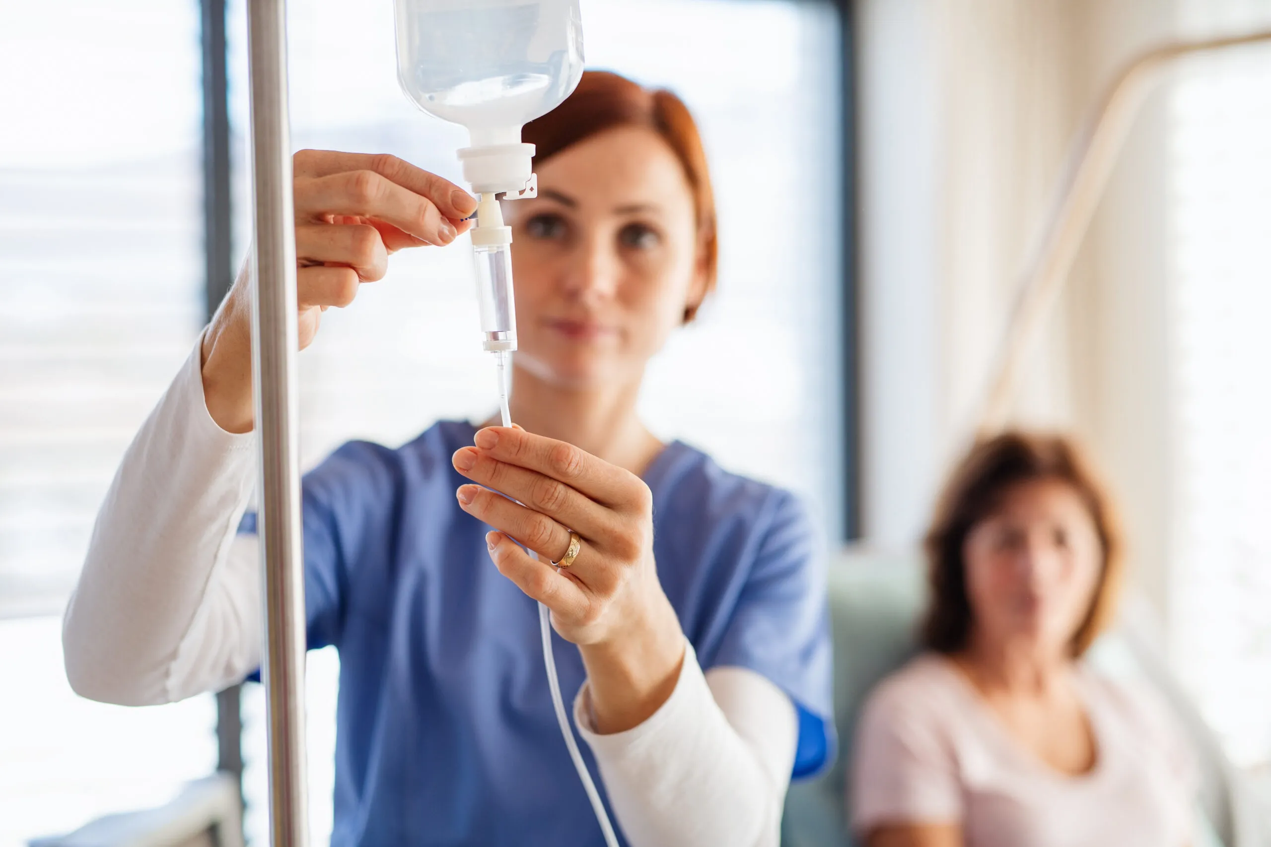 A nurse with IV drip and patient in bed in hospital room- Vitals Health Care